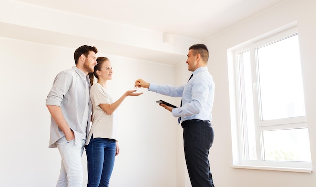 hypotheek, mensen en onroerend goed concept - makelaar geeft sleutels van een nieuw appartement of huis aan een gelukkig stel