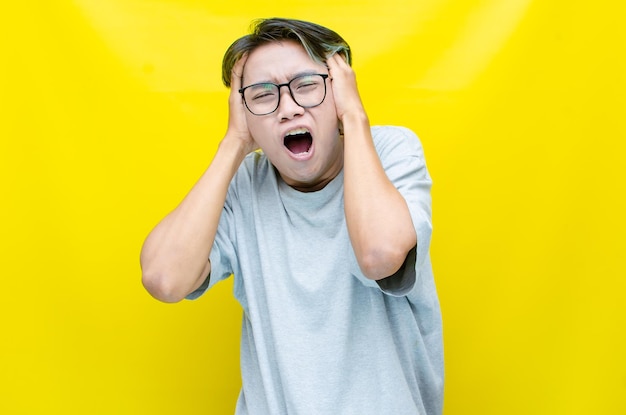 Hysterical mad depressed asian young man covers ears by hand shouts and screams heavyly