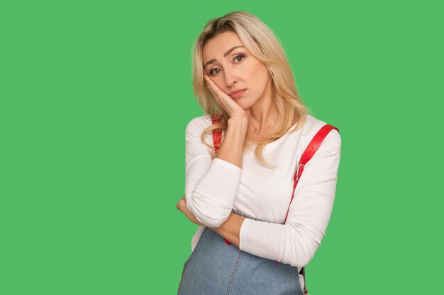 I am bored. Portrait of lazy depressed adult woman in denim overalls leaning on hand and looking with disinterest, feeling tired and indifferent to tedious dull talk. indoor studio shot, isolated