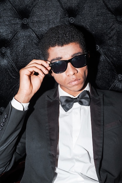 i am a boss here! fashionable young afro-american man sitting on the chair holding hand on glasses