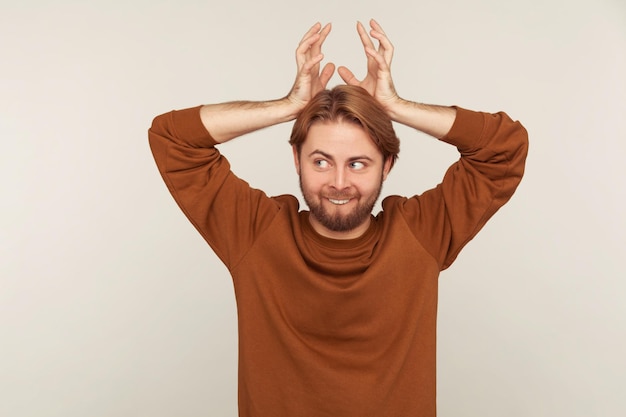 I am deer. portrait of funny childish bearded man in sweatshirt showing antler horns over head and biting teeth