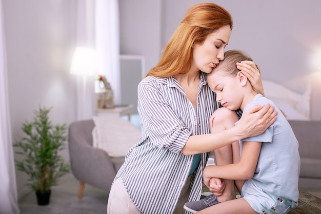 I am with you. Pleasant loving mother kissing her child while sitting together with her