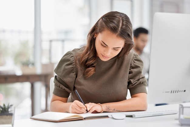 忘れられない。オフィスで働いている間彼女のノートに書いている魅力的な若い実業家のトリミングされたショット。