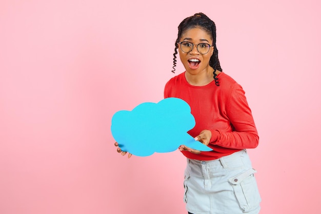 I denk. Peinzende afro-vrouw die naar een lege tekstballon kijkt, haar kin, copyspace, roze studiomuur aanraakt