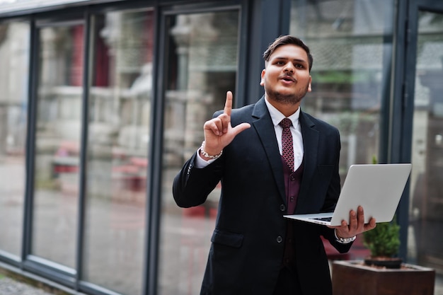 I got idea Stylish indian businessman in formal wear with laptop on hands standing against windows in business center