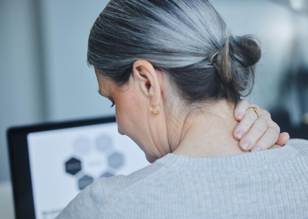 I have a knot in my neck Shot of a mature businesswoman sitting alone in the office and suffering from a sore neck