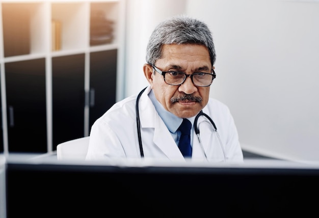 I have my work cut out for me today Cropped shot of a focused mature male doctor working on a computer while being seated in his office during the day