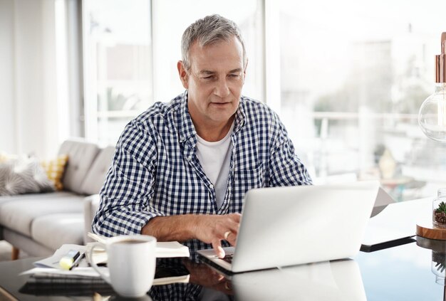 У меня есть несколько электронных писем, чтобы наверстать упущенное Снимок зрелого мужчины, работающего дома за ноутбуком