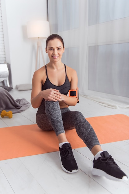 I love fitness. Pretty exuberant athletic dark-haired young woman smiling and exercising while sitting on the carpet