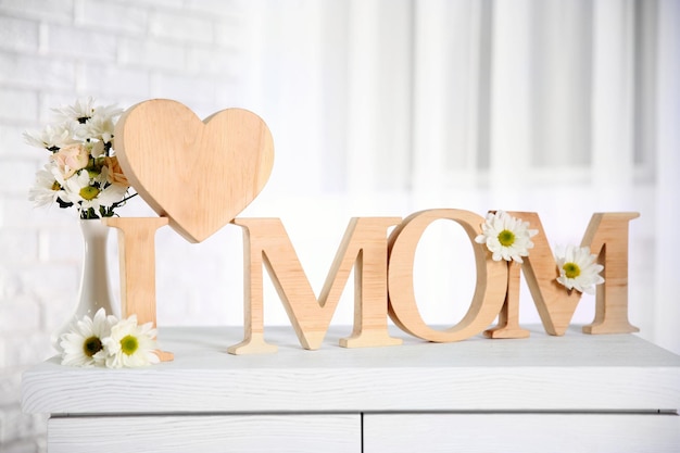 I love mom inscription of wooden letters with heart and flowers on a white table