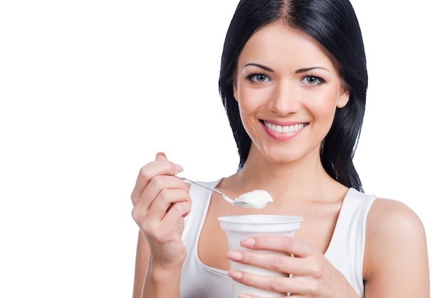 I love mornings. Beautiful young smiling woman holding a spoon with sour cream while standing against white background