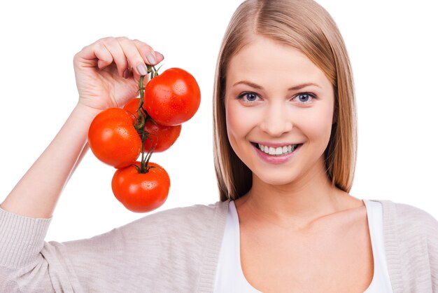 I love tomatoes! Beautiful young woman holding tomatoes and smiling while standing against white background