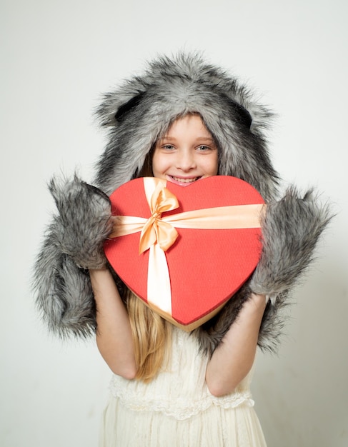 I love you. Small girl wear winter hat scarf. Winter fashion trends for kids. valentines day. present box in shape of heart. red heart. love. boxing day. valentines day shopping. present with love