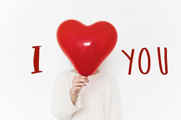 I love you text sign on heart happy valentine\'s day concept\
hand holding red heart balloon on white background with space for\
text greeting card