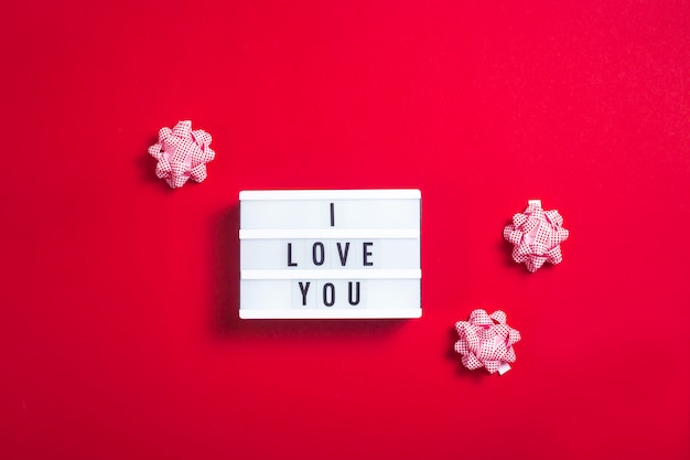 I love you written on a decorative lamp next to the bows for gifts on a bright red background