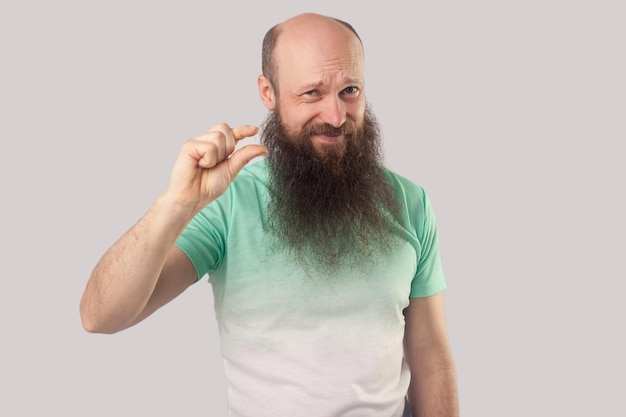 I need a little bit more Portrait of worry middle aged bald man with beard in green tshirt standing looking and pleading for a few something more indoor studio shot isolated on grey background