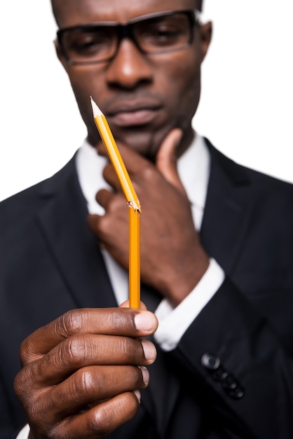 I need a new one. Thoughtful young African man in formalwear holding pencil and looking at it while holding hand on chin and standing isolated on white background