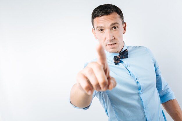 I need you. Serious nice confident man standing against blue background and pointing at you while needing you