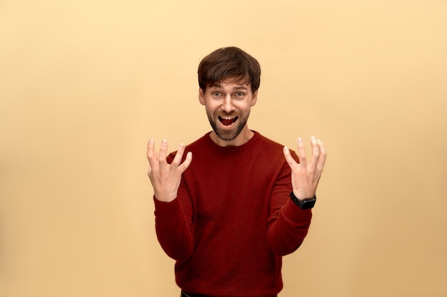 I said no. Photo of young man with beard wearing sweater, gestures angrily, exclaims loudly and has furious expression, posing against beige wall.