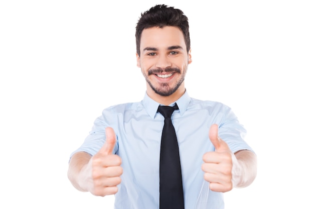 I say yes! Confident young man in shirt and tie looking at camera and showing his thumbs up