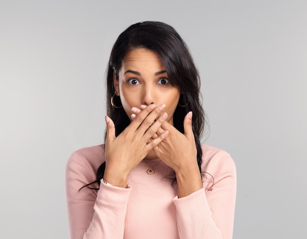 I shouldnt have said that Shot of a beautiful young woman looking surprised while standing against a grey background