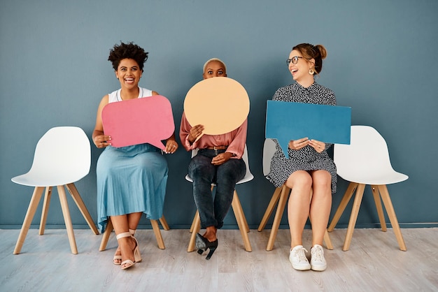 I think I shouldnt have said that Studio shot of a group of attractive young businesswomen holding speech bubbles while sitting in a row against a grey background