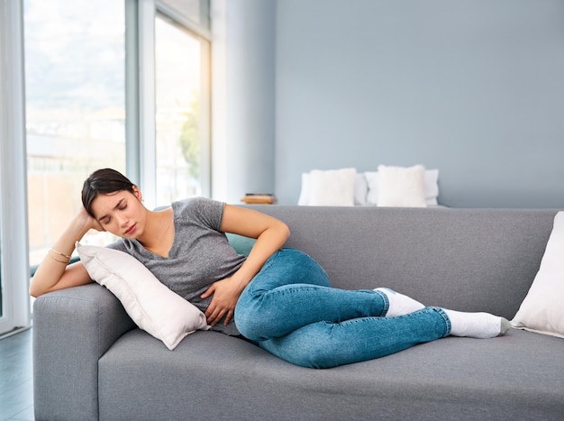 I think Im going to take easy today Shot of a uncomfortable looking young woman holding a water bottle tightly while trying to get rest on a sofa at home