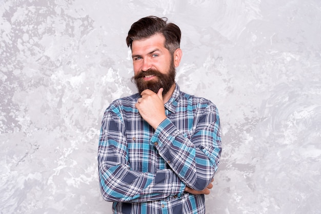 I think so. Confident hipster in checkered shirt. Hipster style. Guy hipster outfit. Mature and trendy. Masculine traits. Brutal bearded man concrete background. Serious man with beard and moustache.