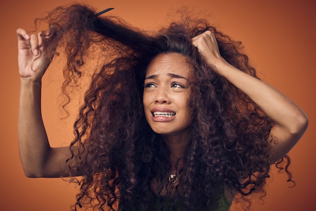 I thought going natural would be less of a struggle Shot of a woman crying while combing our her curls against an orange background