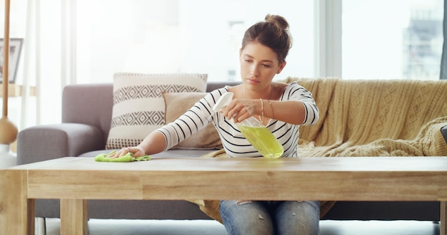 Photo i want this place to be spotless shot of a young woman cleaning the table in her living room