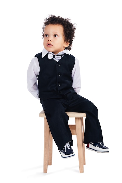 I will just sit here and do nothing! Little African baby boy looking away while sitting on stool against white background