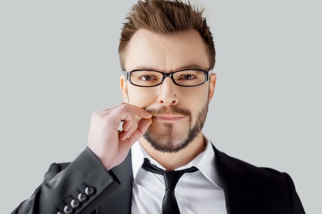 I will say nothing. Portrait of young man in formalwear closing his mouth by hand while standing against grey background