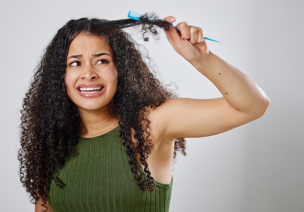 I wish there was a easier way to detangle my hair Shot of a woman frowning while combing her hair against a grey background