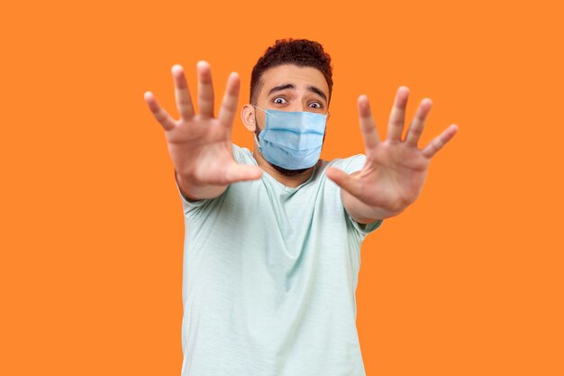 I39m afraid Portrait of scared terrified man with medical mask in white tshirt making frightened gesture with raised hands panic attack concept indoor studio shot isolated on orange background