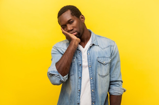 I39m bored portrait of tired disinterested man in denim casual shirt holding head on hand looking with sleepy indifferent expression laziness indoor studio shot isolated on yellow background