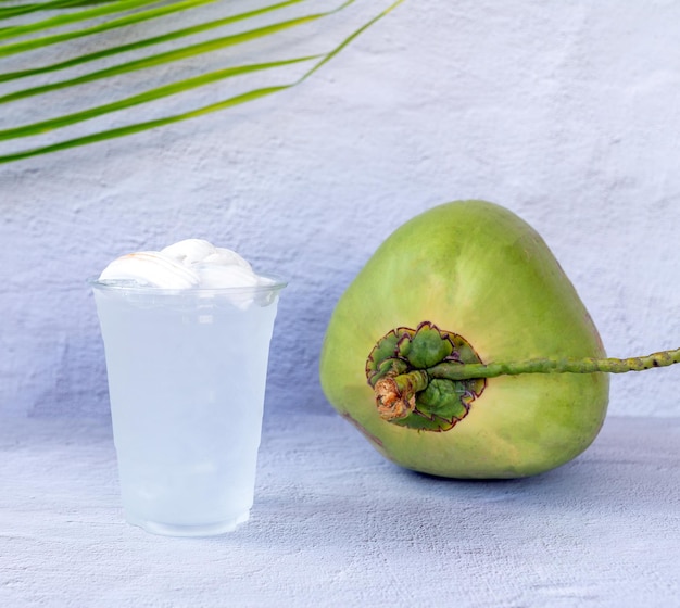 Ледяной кокосовый напиток в пластиковом стакане и кокос на белом фоне