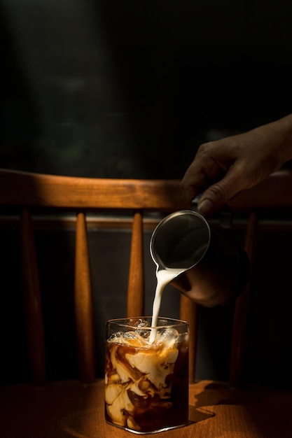 Ice coffee on a black table with cream being poured into it showing the texture