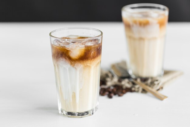 Caffè ghiacciato in un bicchiere con crema sopra e chicchi di caffè sul tavolo