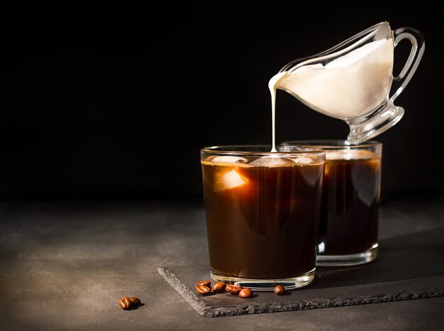 Ice coffee in a glass with cream poured over. gravy boat with milk levitates.