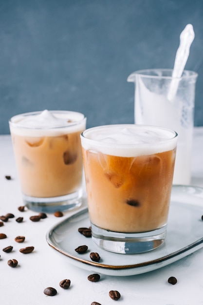 Ice coffee in glass with milk foam and ice cubes, coffee beans on white table