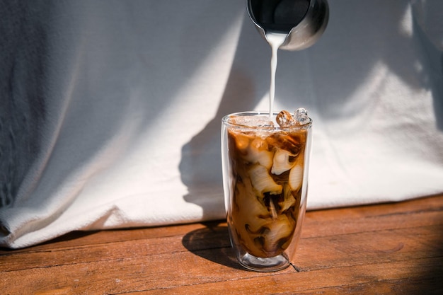 Ice coffee on a table with cream being poured into it showing the texture