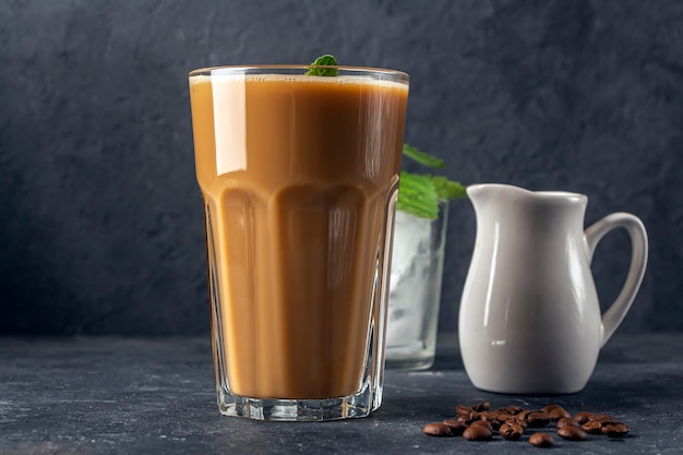 Ice coffee with mint and milk. Big glass of coffee cocktail and glass with ice cubes. Cool refreshment summer drink on dark background in law key. copy space for text.