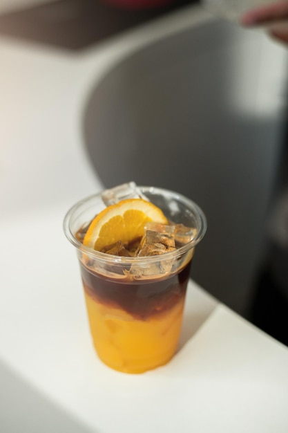 Ice coffee with orange on a plastic cup with cream being poured into it showing the texture