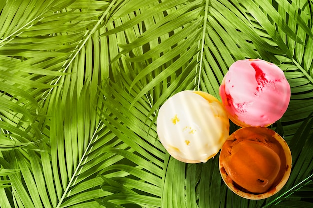 Ice cream of chocolate, vanilla, and strawberry with palm leaves view