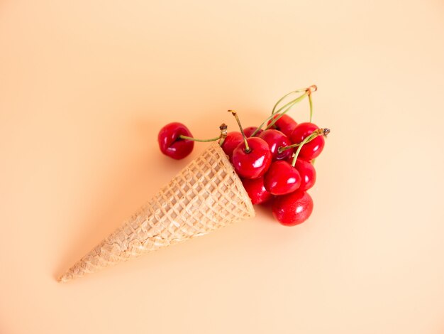 Ice cream cone and fresh cherries on light pink background