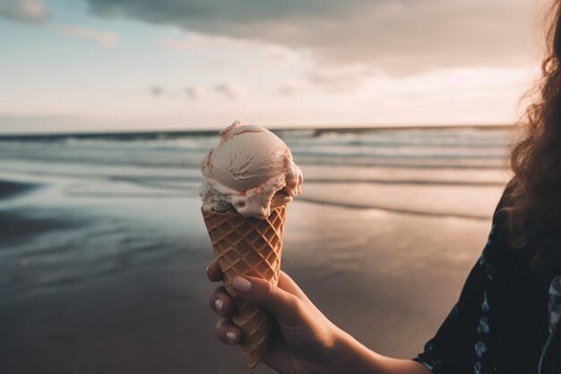 An ice cream cone in hand while standing on a sandy beach with ocean waves in the background