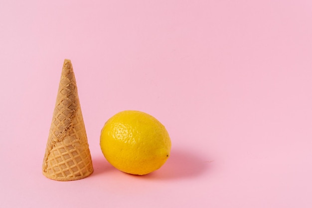 Ice cream cone and lemon fruit on a light pink background.