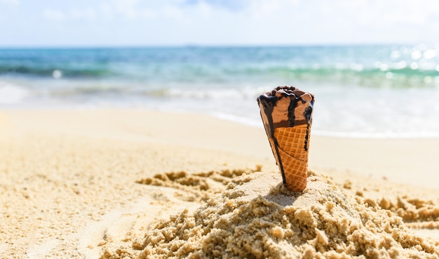 砂のビーチの背景にアイスクリームコーン-夏の暑い天気の海の風景自然の屋外の休暇、アイスクリームチョコレートのビーチの海でアイスクリームを溶かす