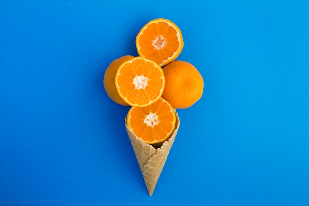 Photo ice cream cone with chopped tangerines in the center of the blue table. top view. copy space.