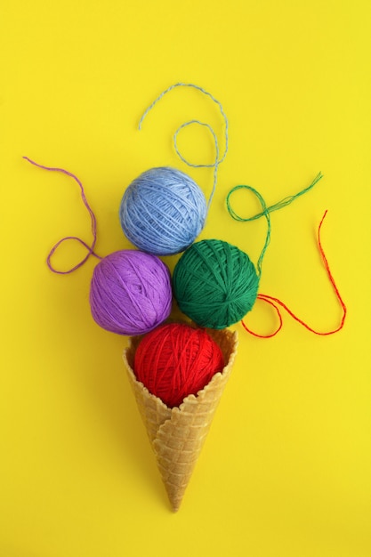 Foto cono gelato con fili colorati per lavorare a maglia al centro della superficie gialla. vista dall'alto. copia spazio. posizione verticale.